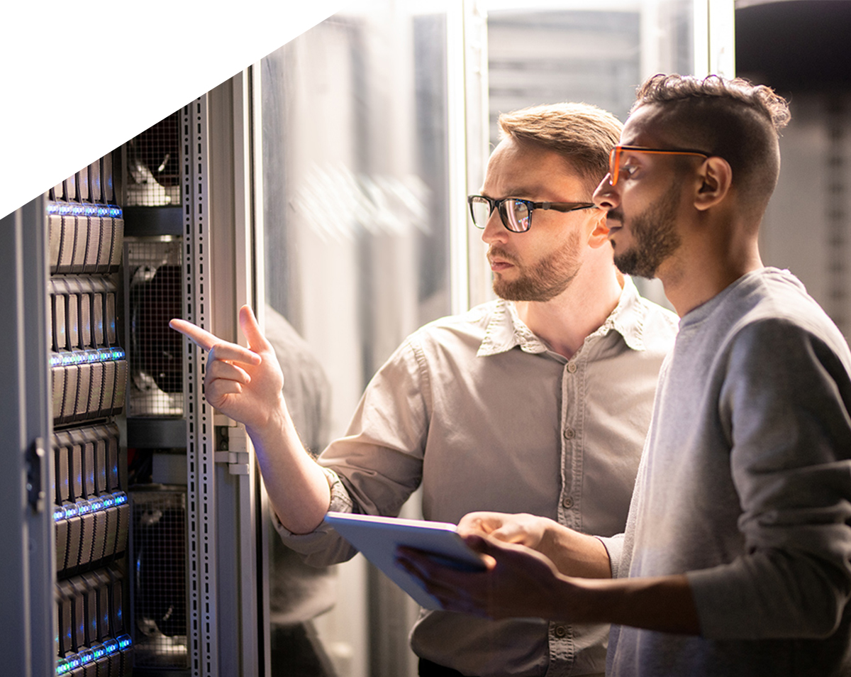 Team-of-young-multi-ethnic-specialists-in-glasses-standing-at-server-and-using-tablet-while-managing-network-server-together-in-data-center-1